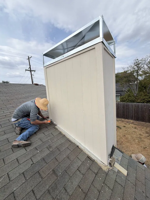 Crew member fitting trim at the base of a newly sided chimney chase on a roof